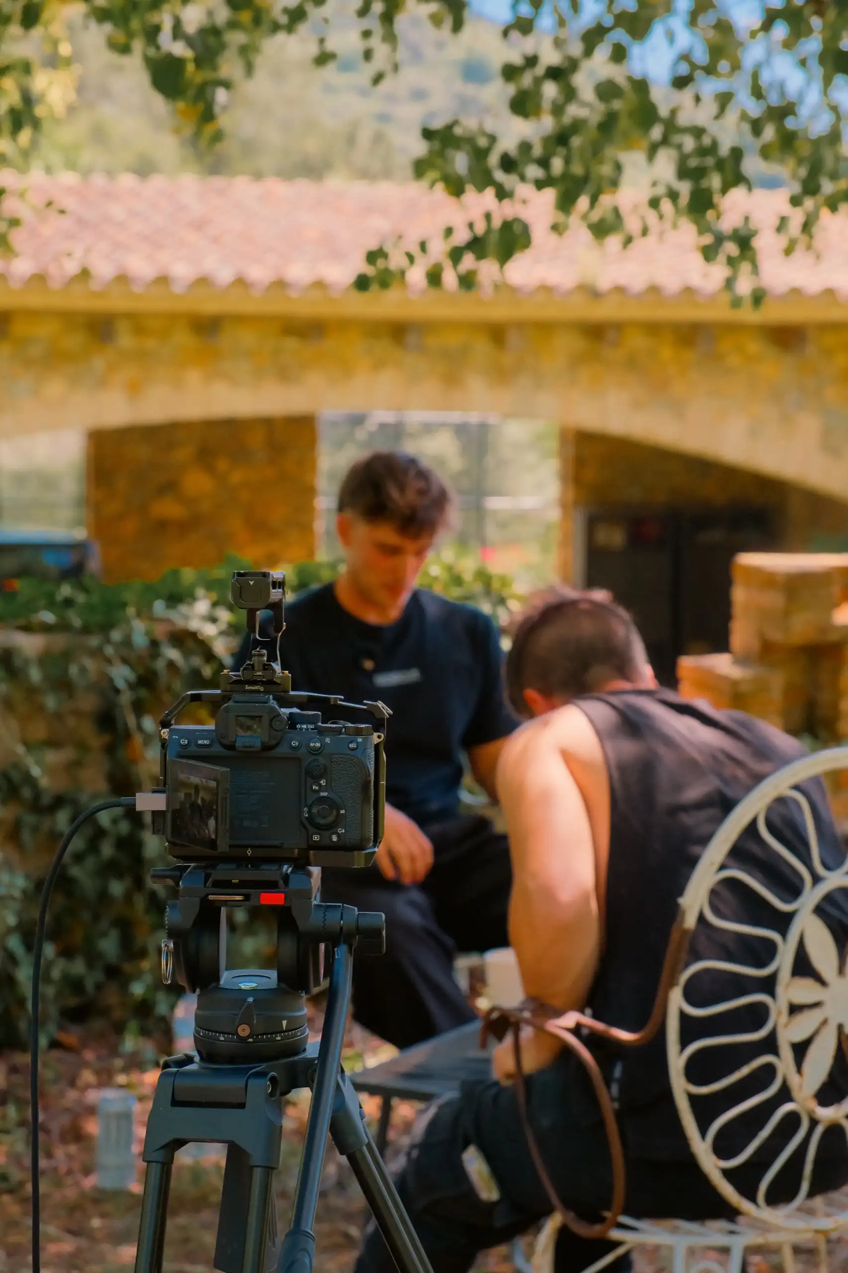 Càmera darrere l’entrevistador, amb el convidat al davant i la masia al fons