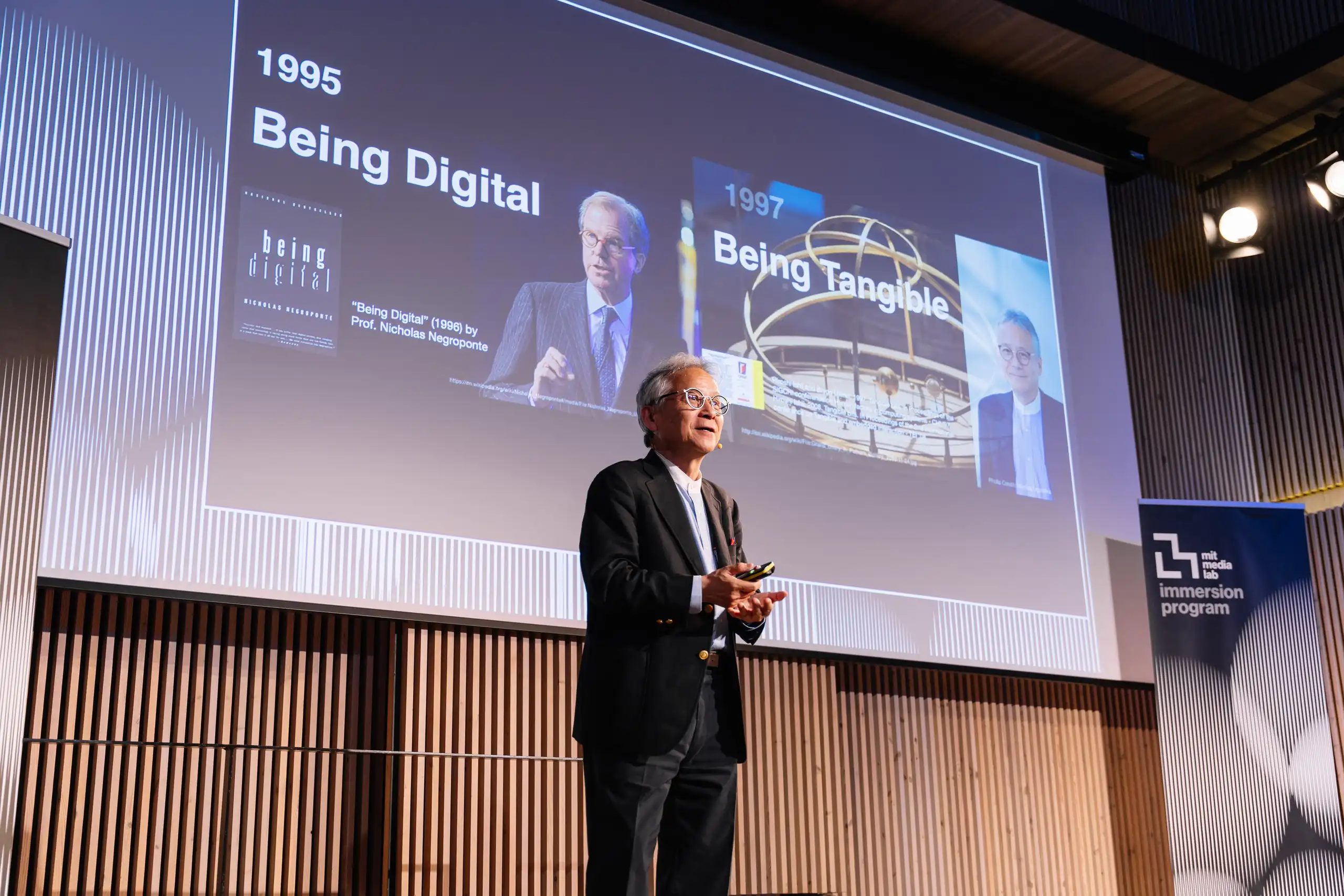 Un ponent parla davant una pantalla que projecta «Being Digital», de 1995