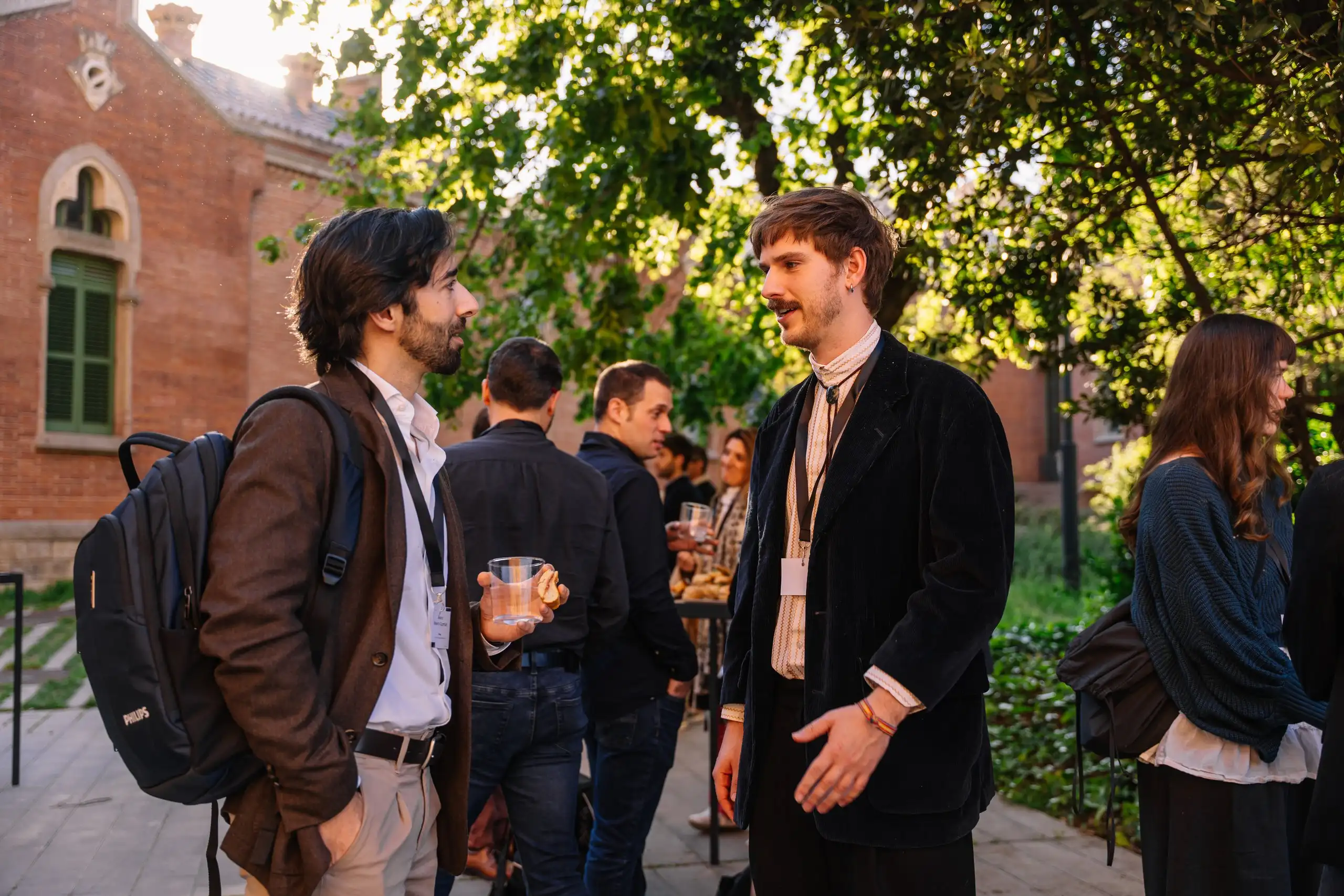 Assistents conversen en un jardí, davant d’un edifici de maó
