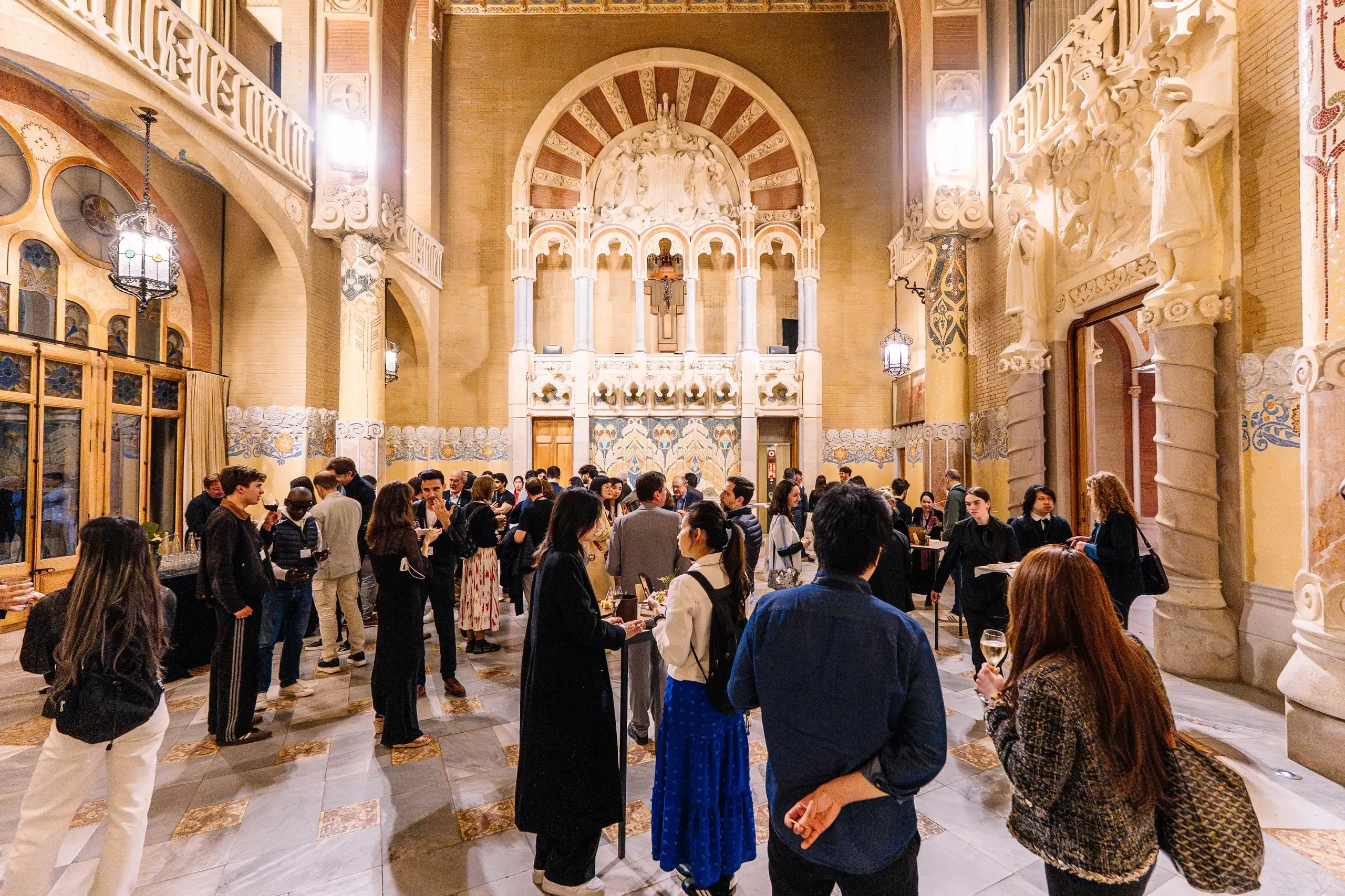 Grup d’assistents en una sala modernista amb arcs i decoració daurada