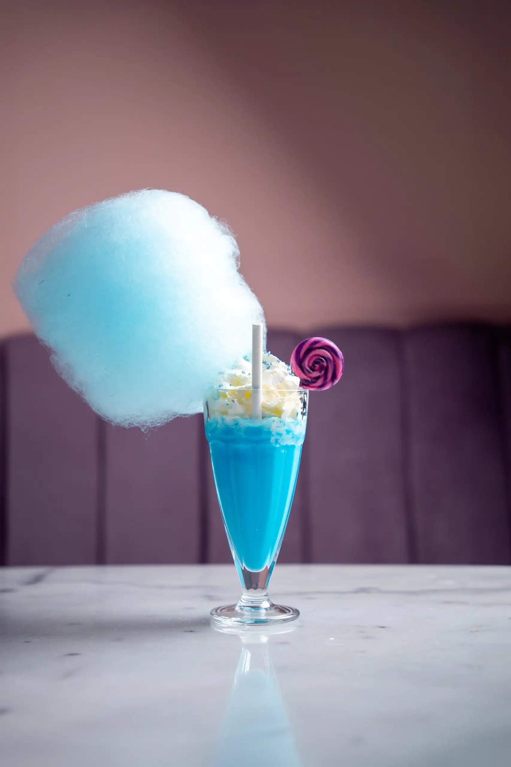 Batut blau amb cotó de sucre i una piruleta, sobre una taula de marbre