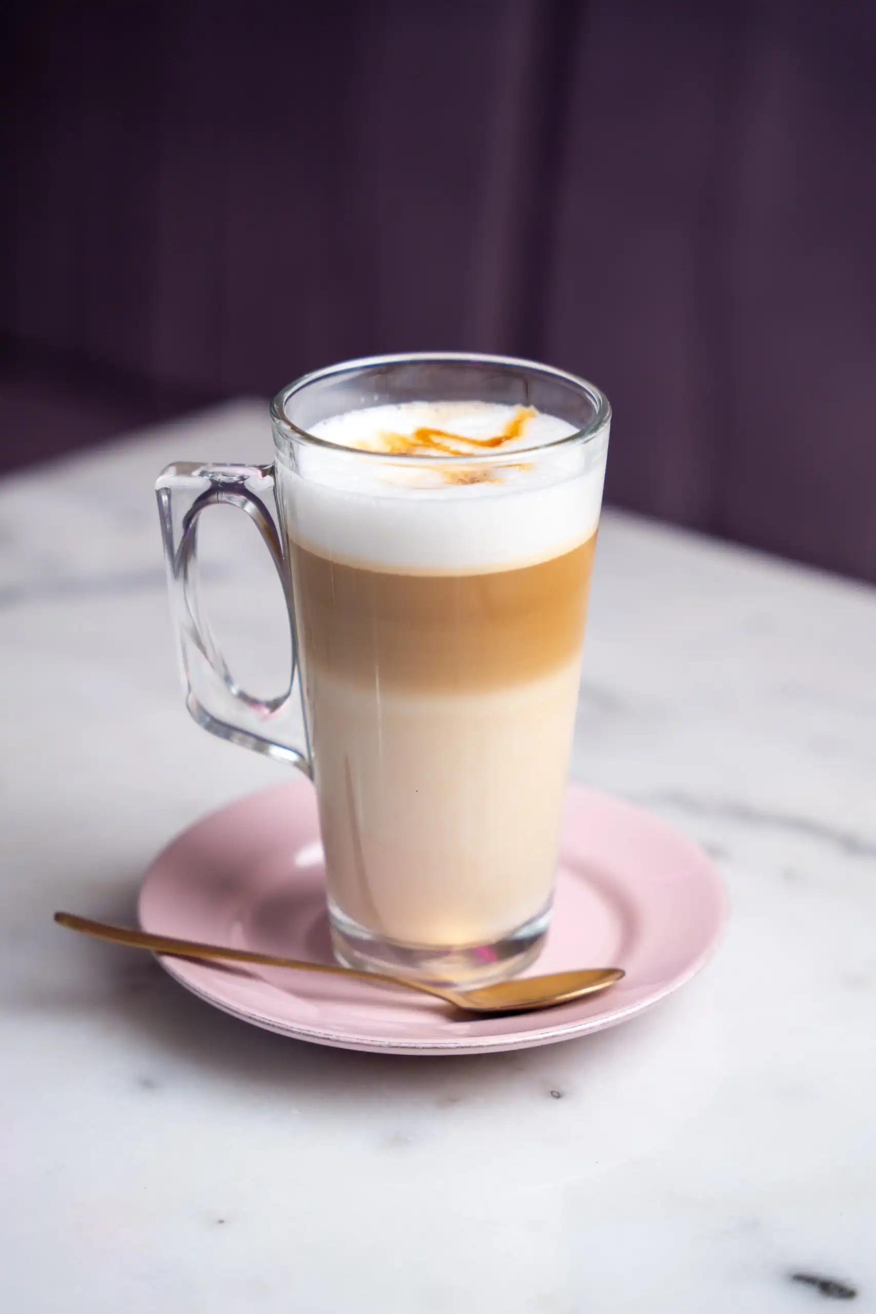Caramel latte en got de vidre sobre un plat rosa, amb una cullereta daurada