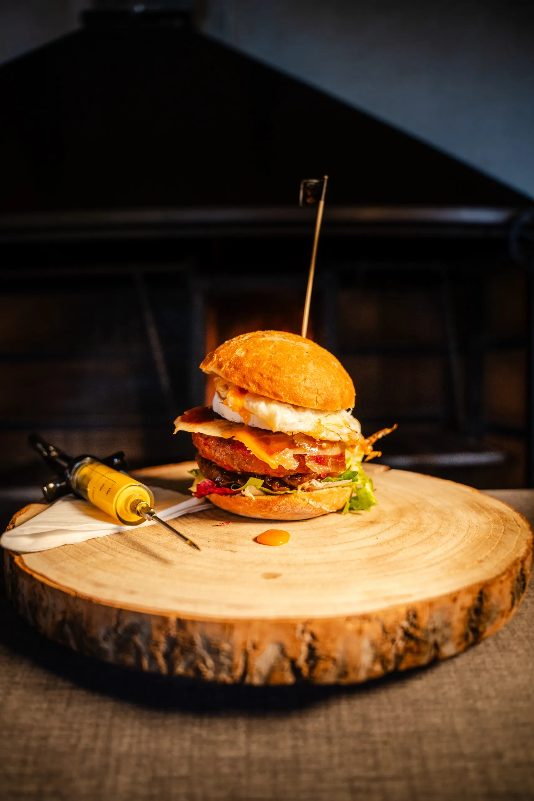 Hamburguesa con huevo sobre tabla de madera, con la brasa encendida detrás