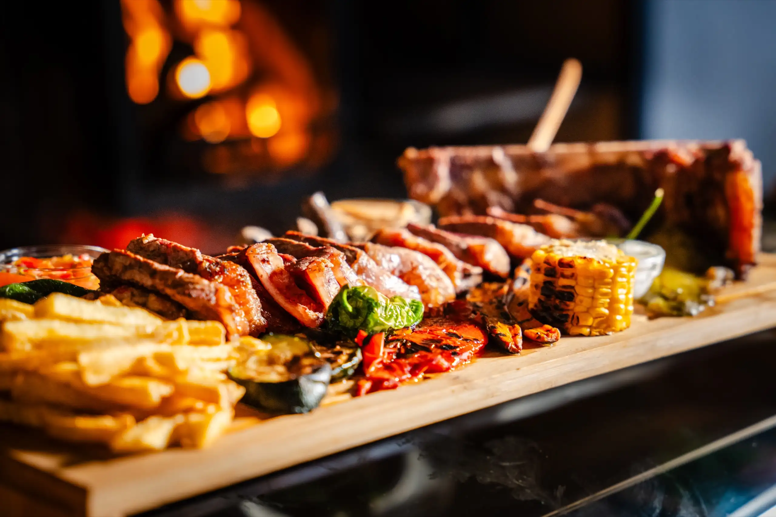 Parrillada de carne y verduras sobre tabla, delante del fuego