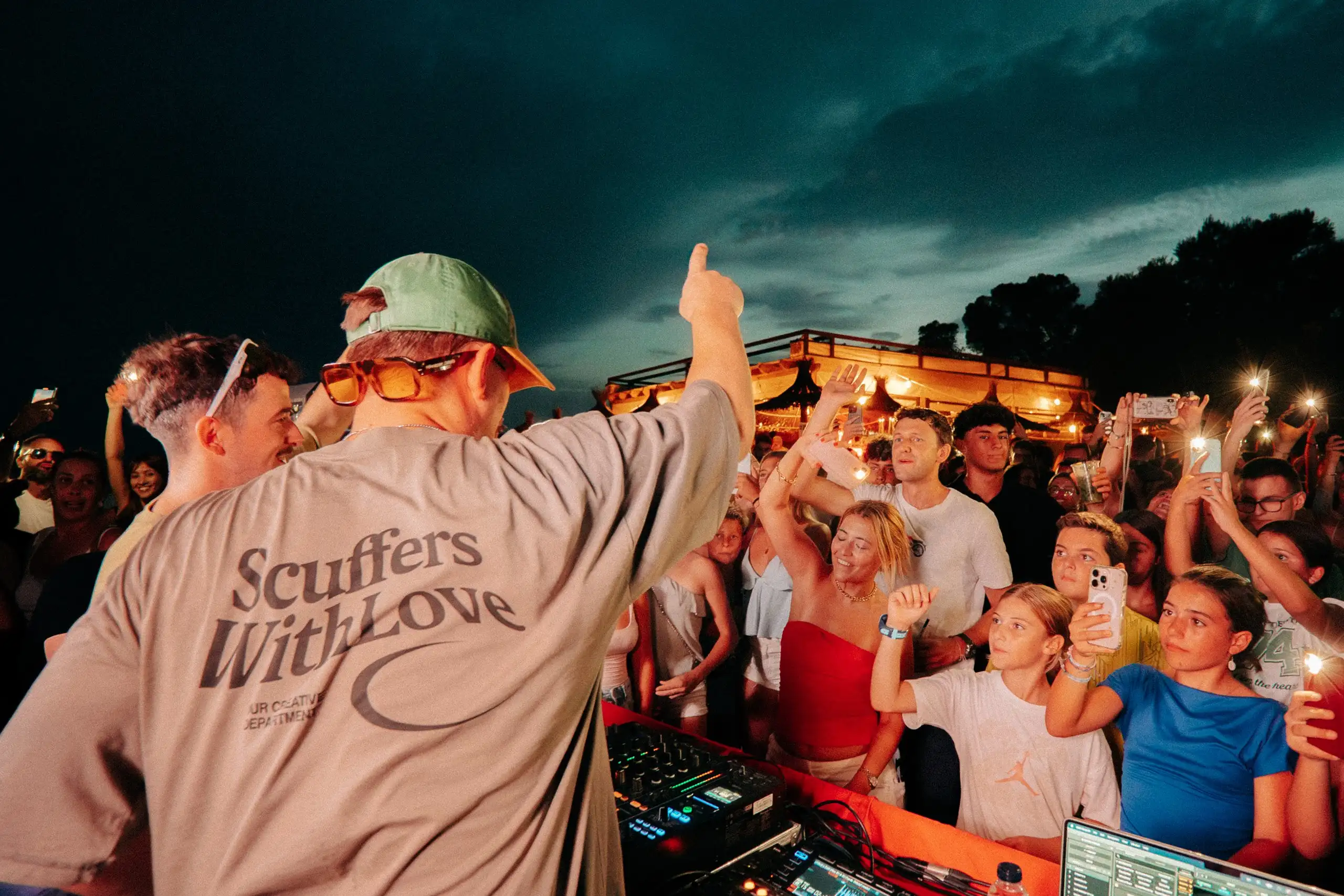 Un DJ d’esquena davant el públic, que il·lumina la nit amb els llums dels mòbils